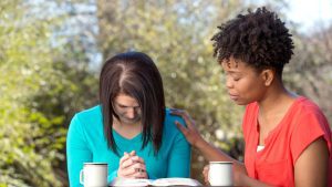 Woman compassionately supporting a friend with these 7 trauma healing scriptures as she reads her bible 